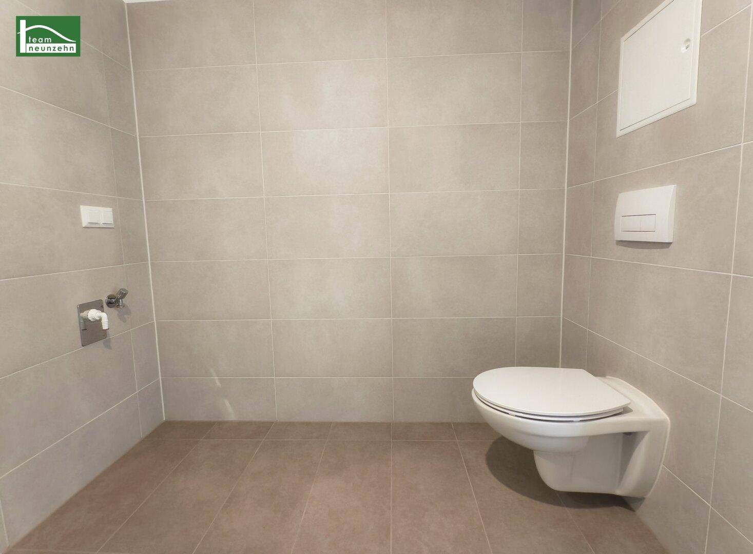 Separates WC mit modernen grauen Fliesen und wandhängender Toilette, in neuwertigem Zustand.