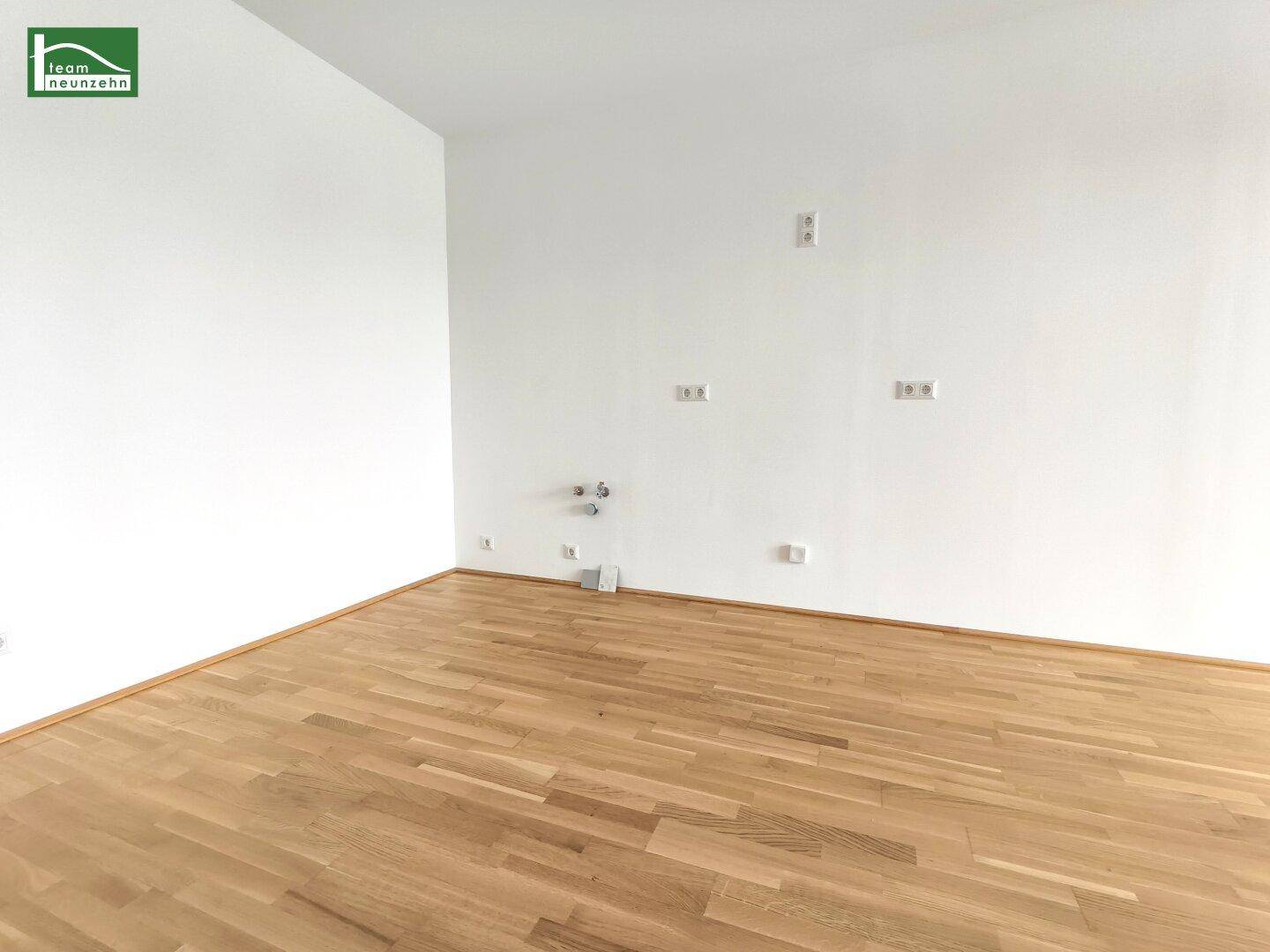 Leerer Küchenbereich mit vorbereiteten Anschlüssen und hellem Parkettboden, ideal für eine Einbauküche.