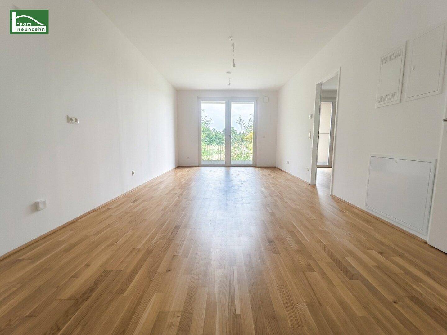 Helles, leeres Wohnzimmer mit Eichenparkett und großen Fenstertüren zum Balkon.