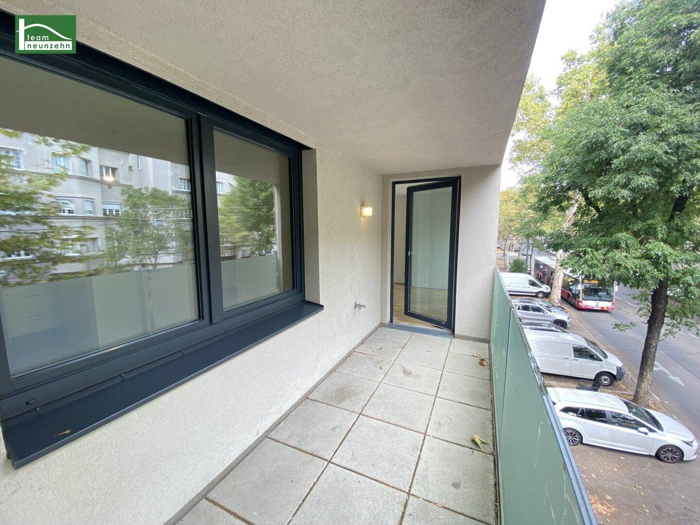 Schmaler Balkon mit Fliesenboden und Blick auf die Straße und Bäume.