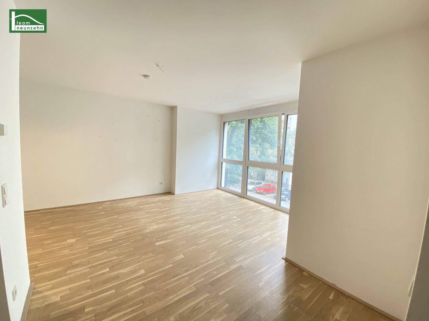Geräumiges Wohnzimmer mit hellem Parkettboden und großen Fenstern zur Straßenseite.