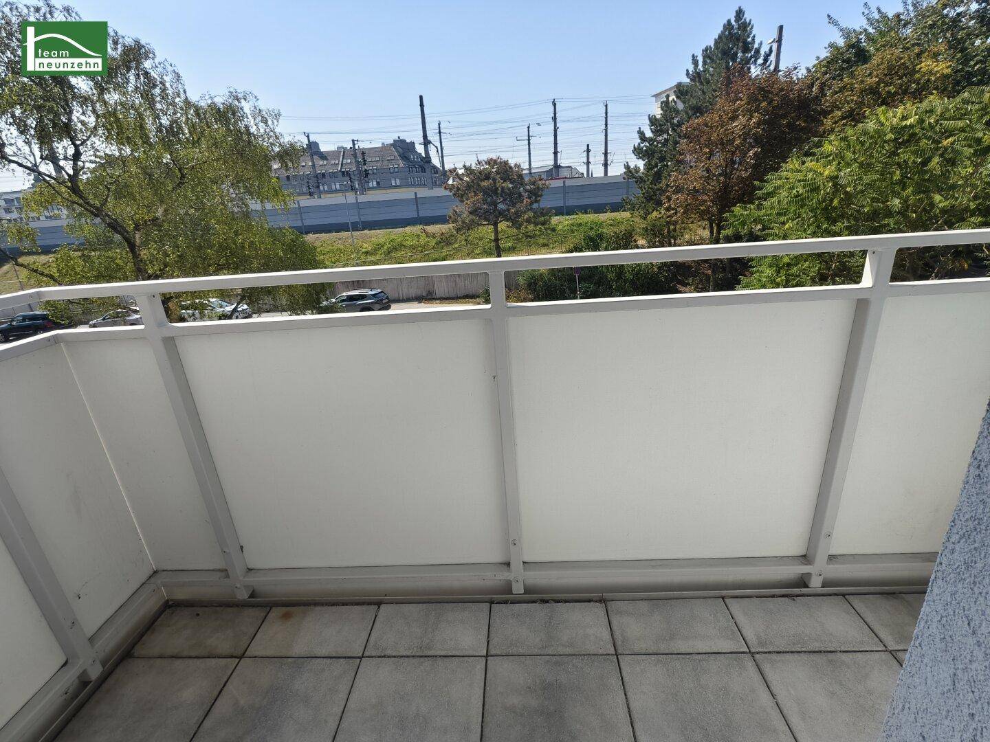 Balkon mit Fliesenboden und Blick auf die Umgebung mit Bäumen und Bahngleisen.