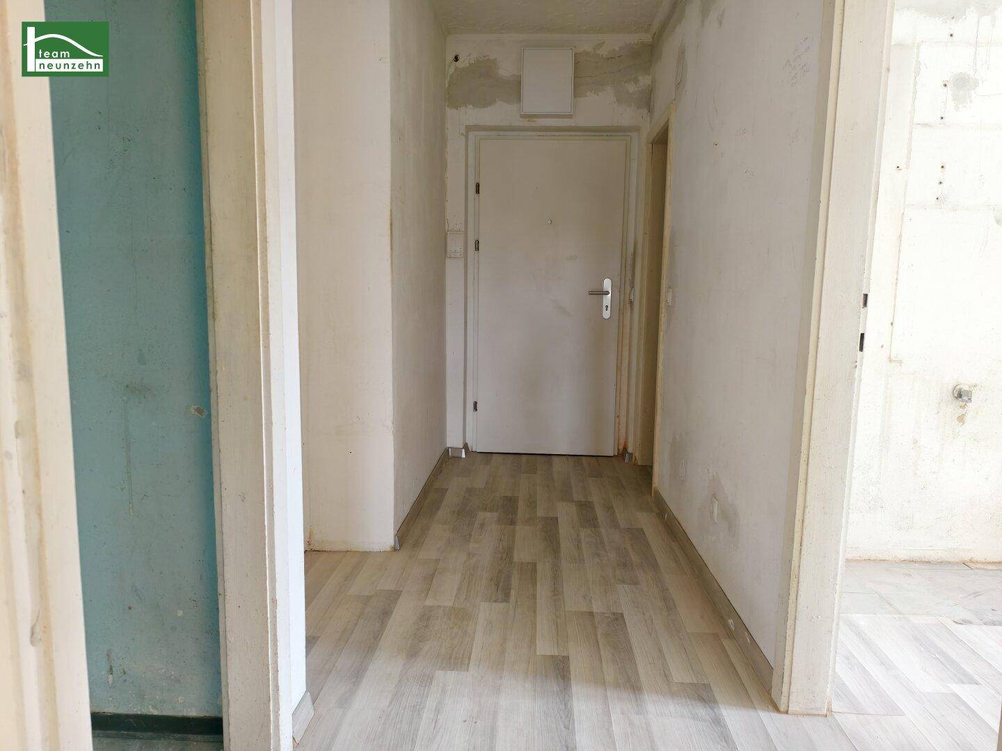 Schmaler Flur mit hellem Laminatboden und Türen zu verschiedenen Räumen.