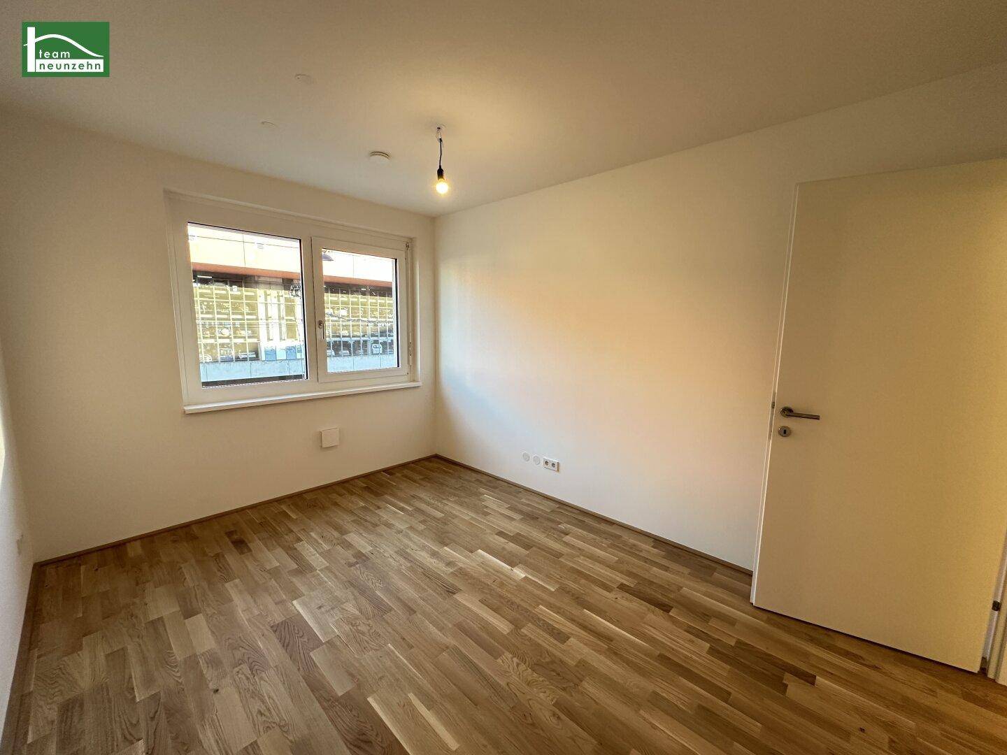 Unmöbliertes Zimmer mit Holzboden und weißer Tür, bereit zur individuellen Gestaltung.