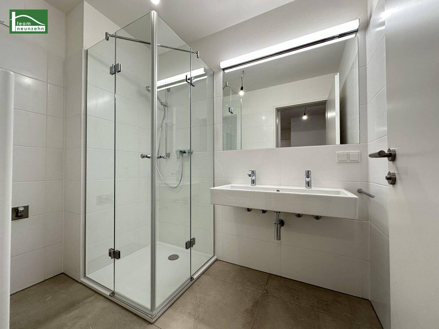 Modernes Badezimmer mit großer Glasdusche und Doppelwaschbecken, hell gefliest.