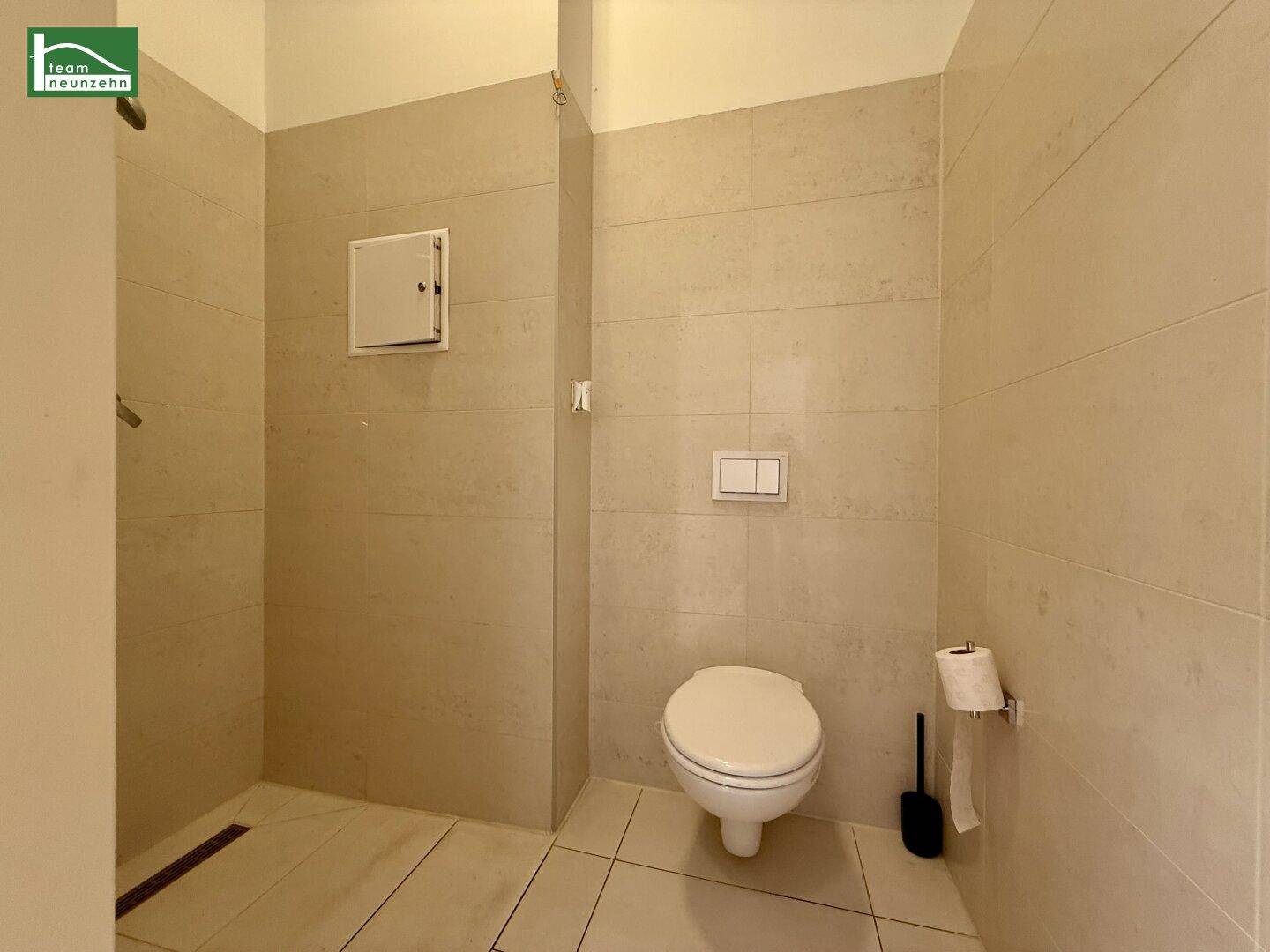 Separate Toilette mit wandhängendem WC und gefliesten Wänden, angrenzend an einen Duschbereich.