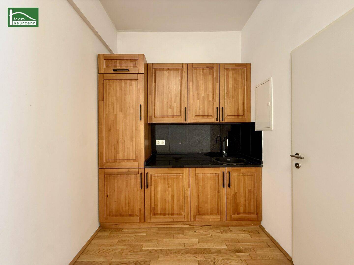 Funktionale Küchenzeile mit Holzschränken, schwarzer Arbeitsplatte und Spülbecken in einem kleinen Raum.