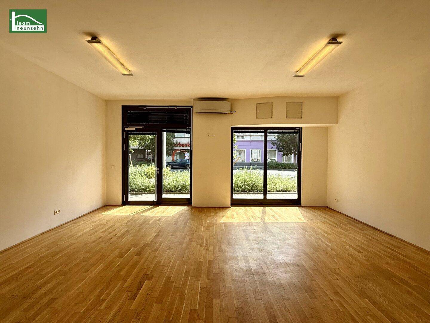 Heller Gewerberaum mit Holzboden, großen Glasfronten und Klimaanlage, ideal für Laden oder Büro.