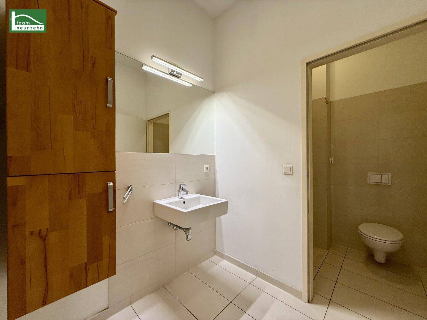 Modernes Badezimmer mit Waschbecken, großem Spiegel und Holzschrank, angrenzend an eine Toilette.