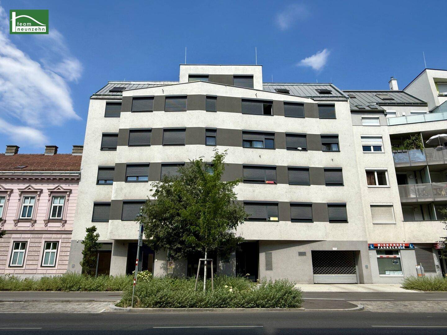 Modernes Mehrfamilienhaus mit grauer und weißer Fassade, vielen Fenstern und dunklen Rollläden.