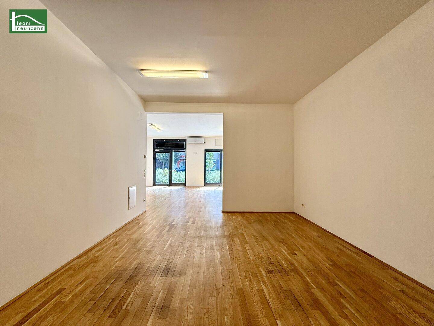 Geräumiger, leerer Gewerberaum mit Holzboden und Blick in einen weiteren Bereich.