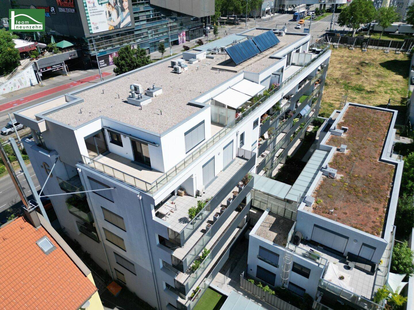 Moderne Wohnanlage mit Flachdach, Photovoltaikanlage und zahlreichen Balkonen sowie Dachterrassen in urbaner Umgebung.
