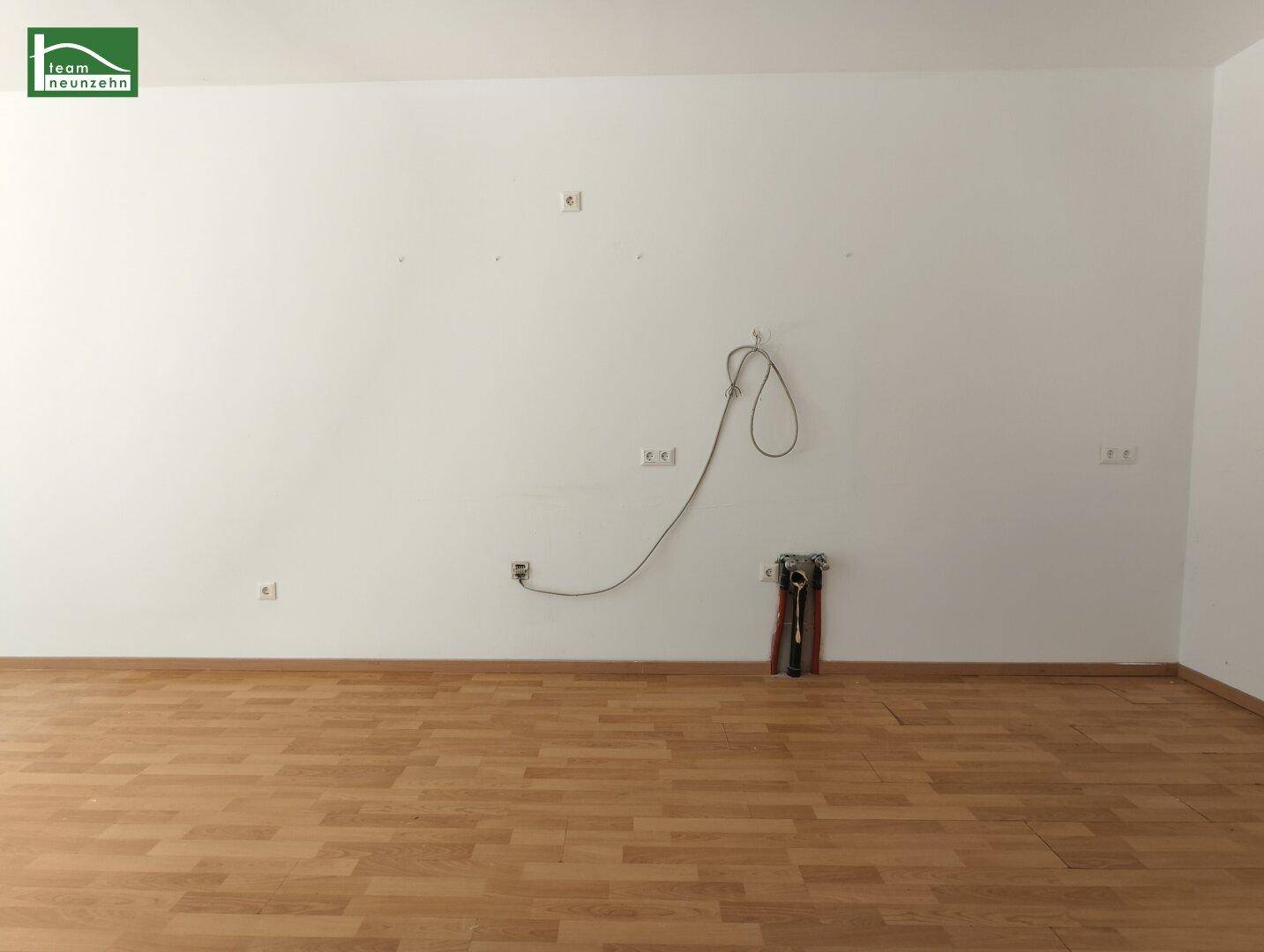 Leerer Küchenbereich mit vorbereiteten Anschlüssen für eine Einbauküche und Holzboden.