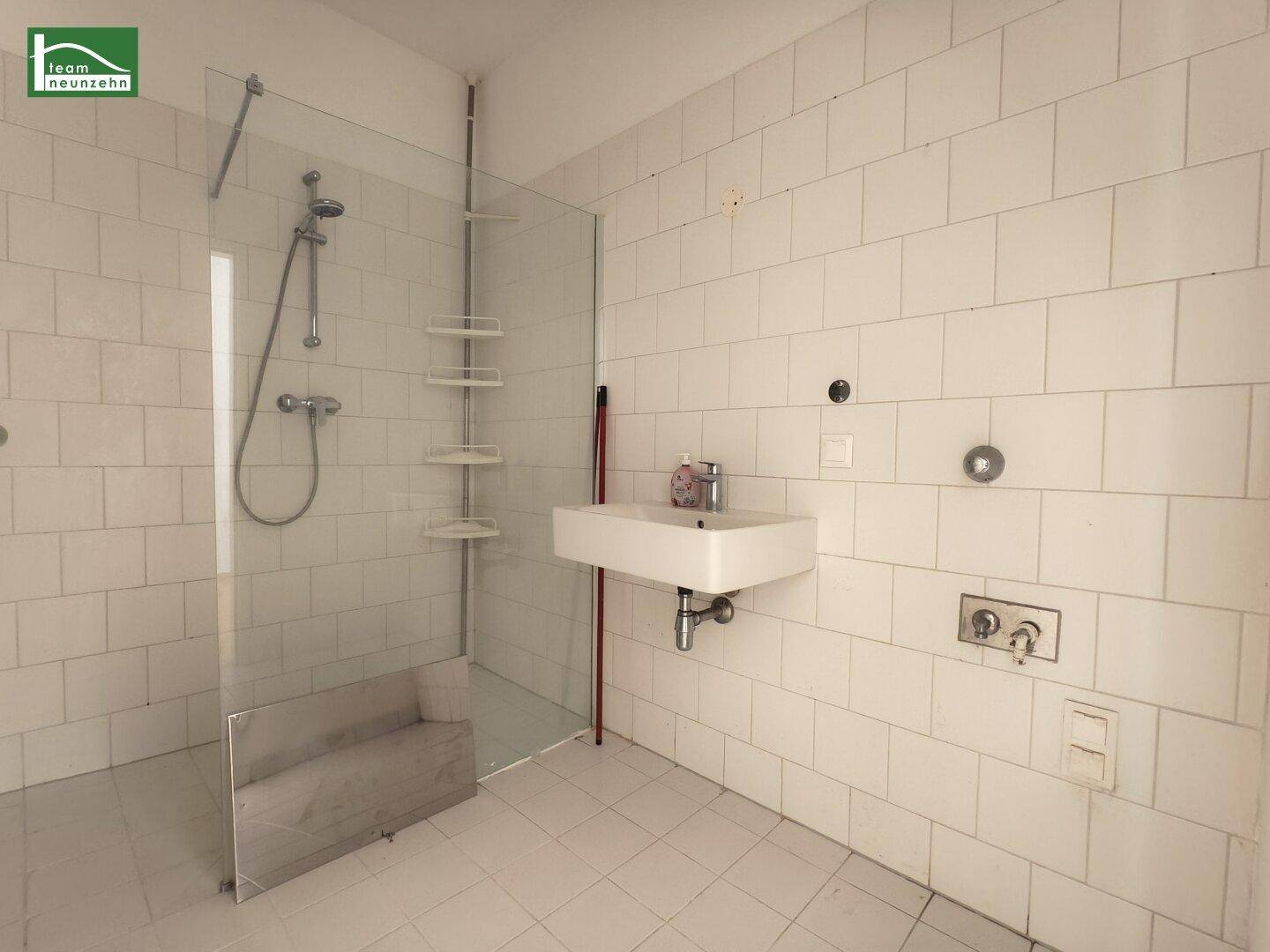 Modernes Badezimmer mit weißen Fliesen, einer begehbaren Dusche und einem wandmontierten Waschbecken.
