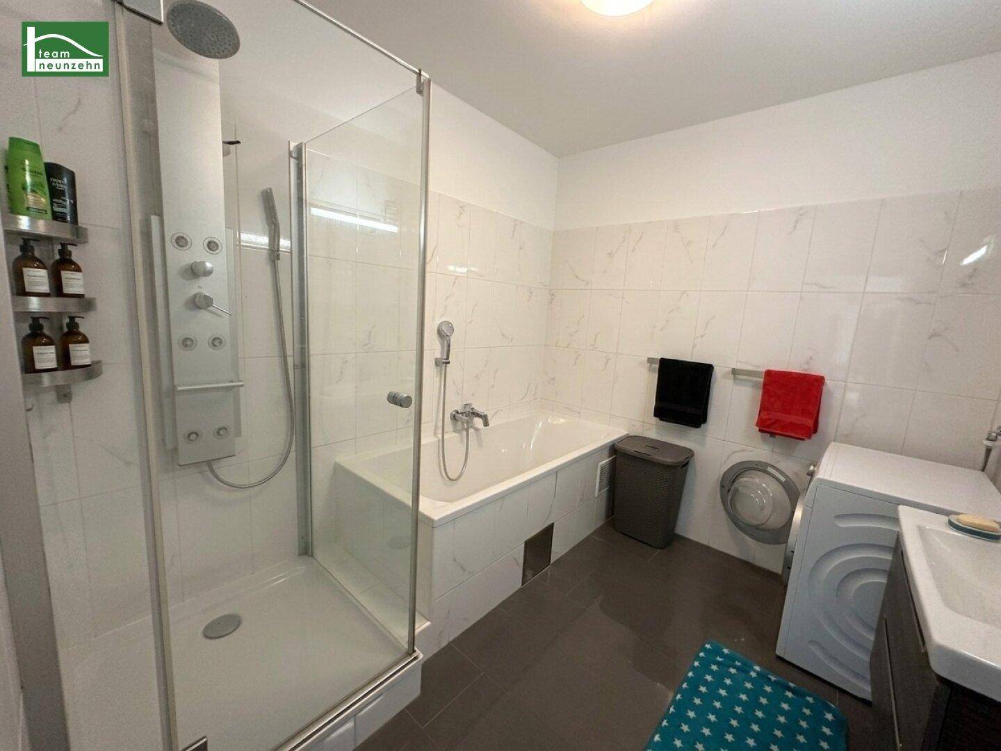 Modernes Badezimmer mit Dusche, Badewanne, Waschmaschine und großformatigen Fliesen.
