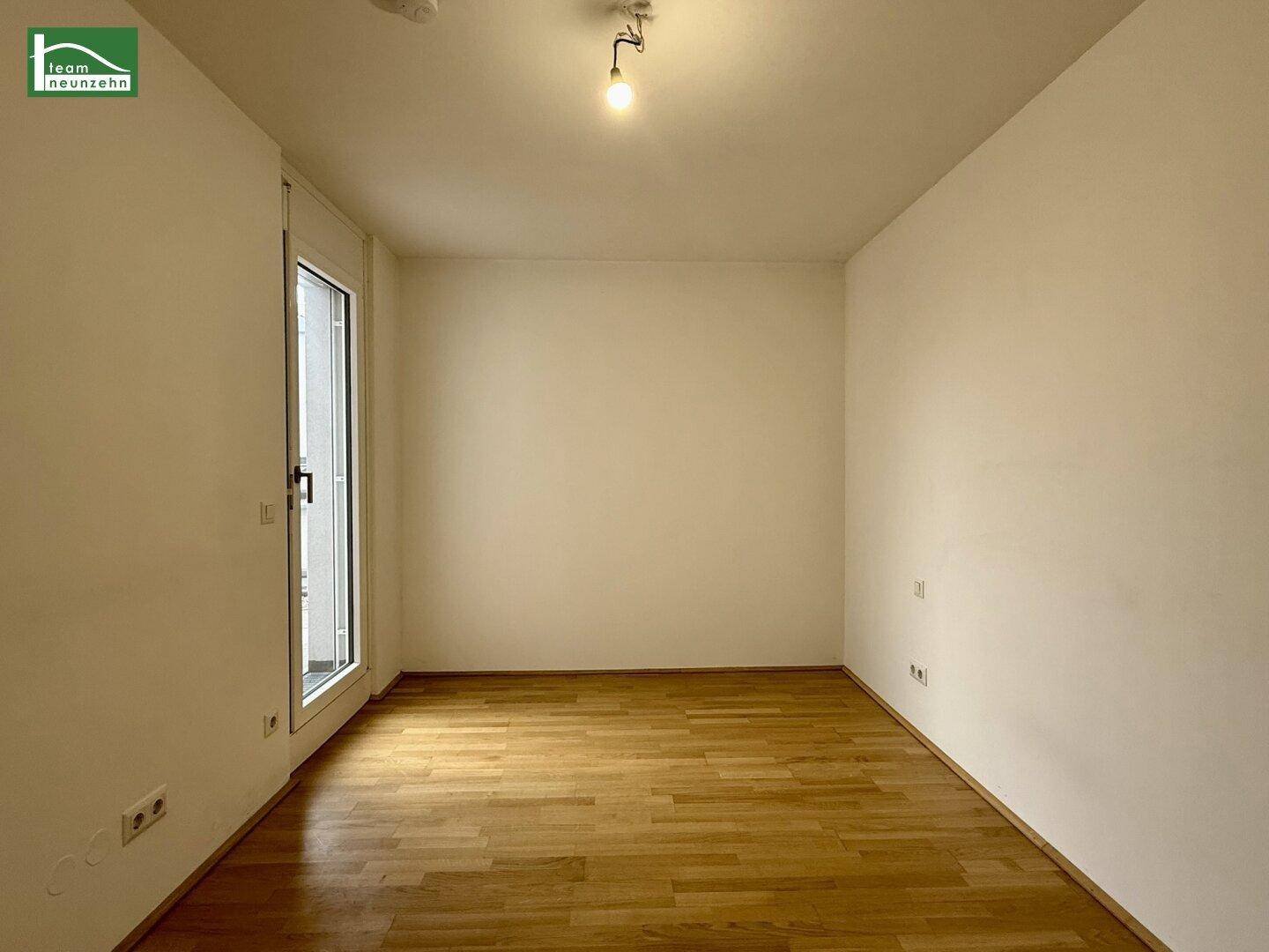Leeres Zimmer mit hellem Parkettboden und Zugang zu einem Balkon oder einer Terrasse.