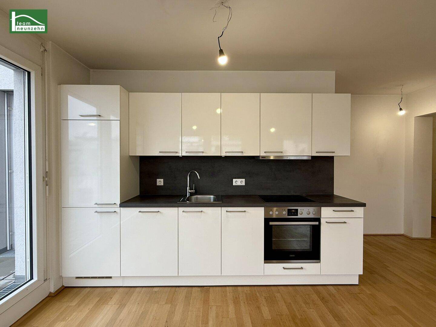 Moderne Einbauküche mit weißen Hochglanzfronten, integriertem Backofen und dunkler Arbeitsplatte.