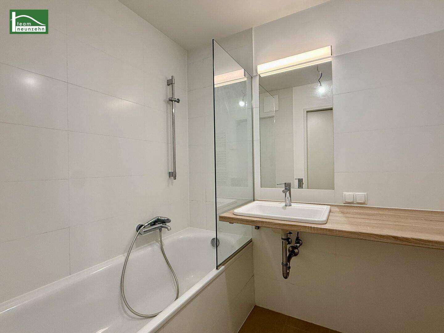 Modernes Badezimmer mit Badewanne, Duschwand und Einzelwaschbecken auf Holzablage.