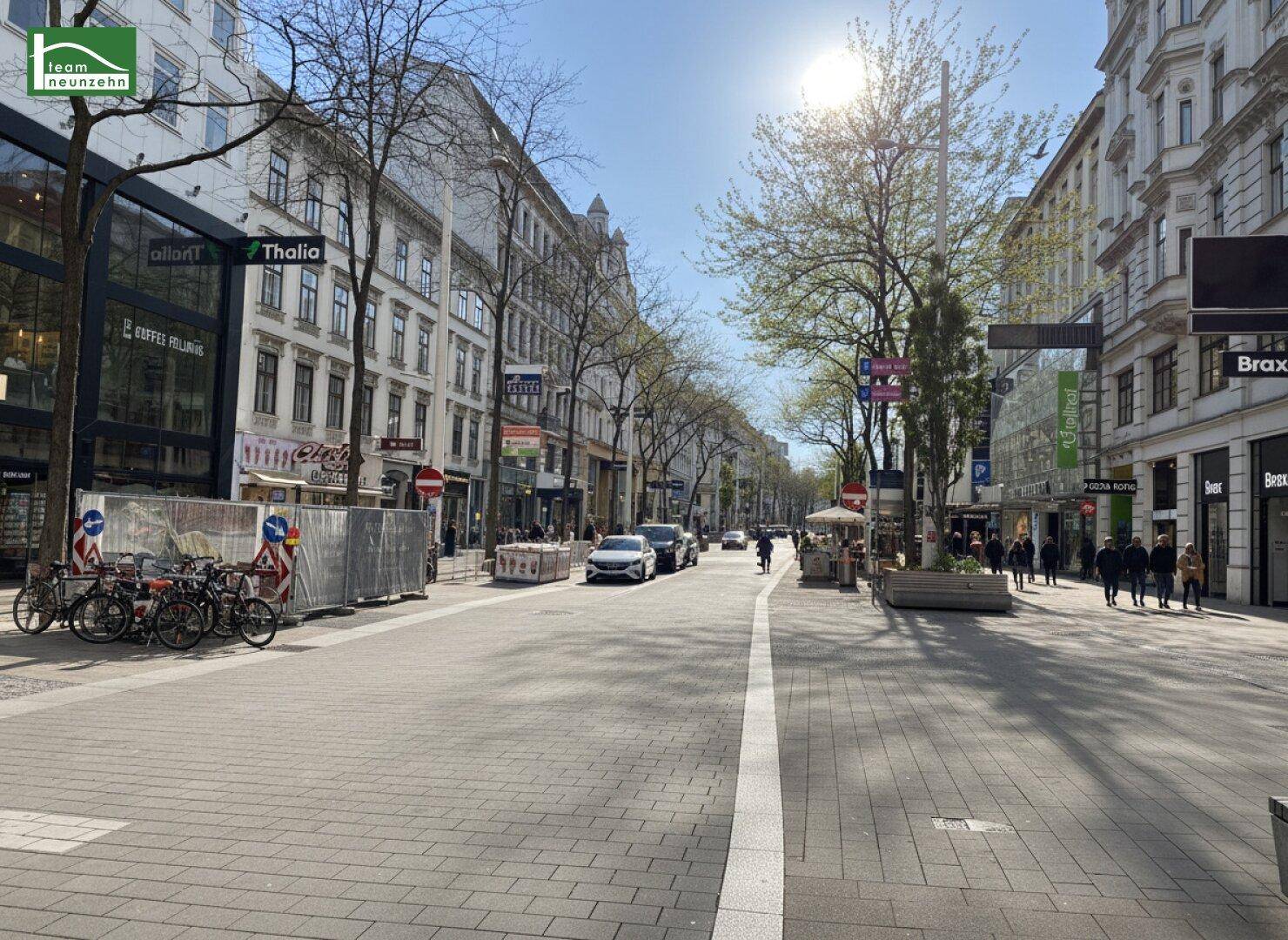 Belebte Einkaufsstraße in der Stadt mit historischen Gebäuden, Geschäften und Fußgängern unter blauem Himmel.