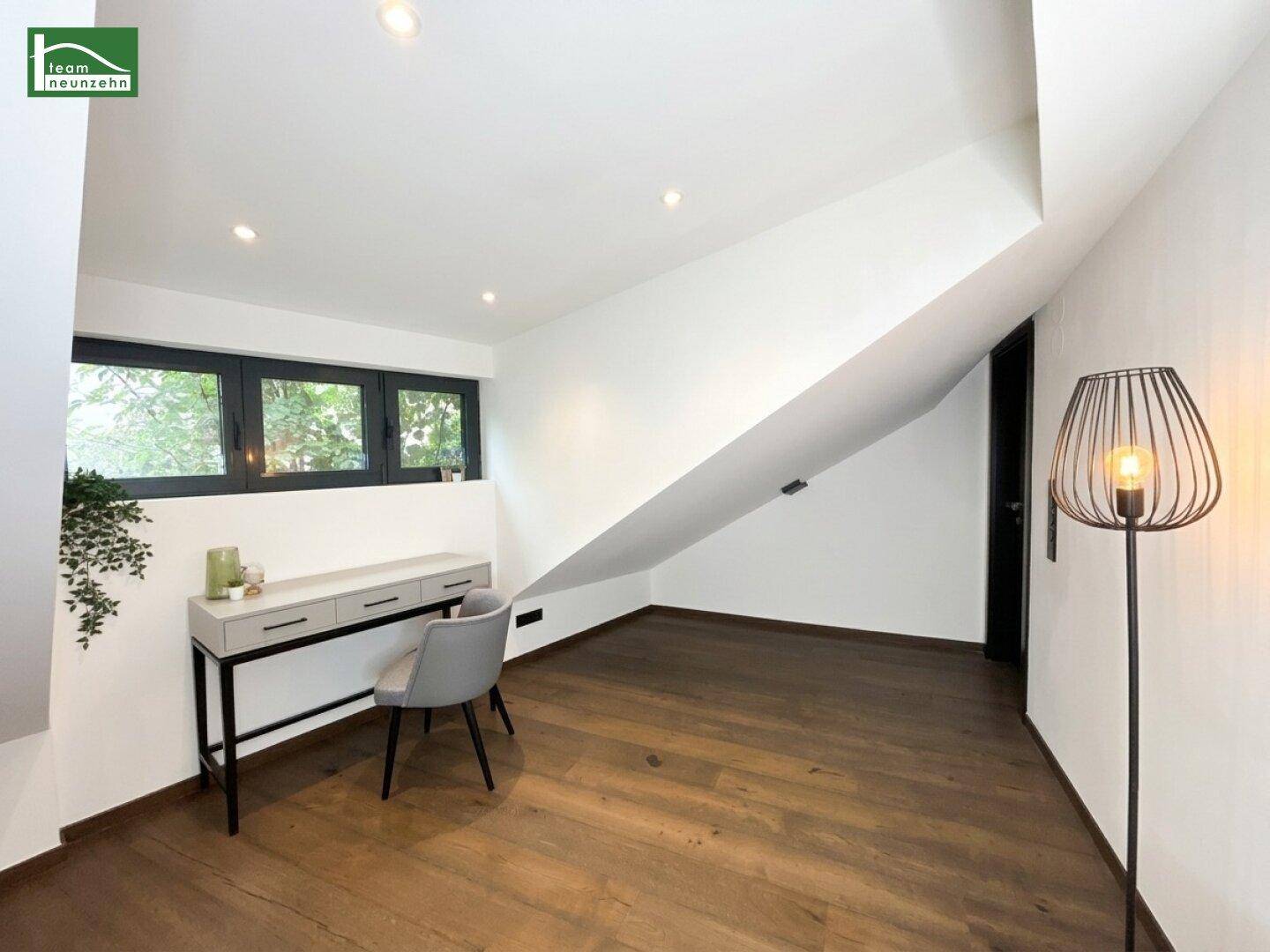 Helles Arbeitszimmer mit Holzboden, Schreibtisch und Fenster mit Blick ins Grüne.