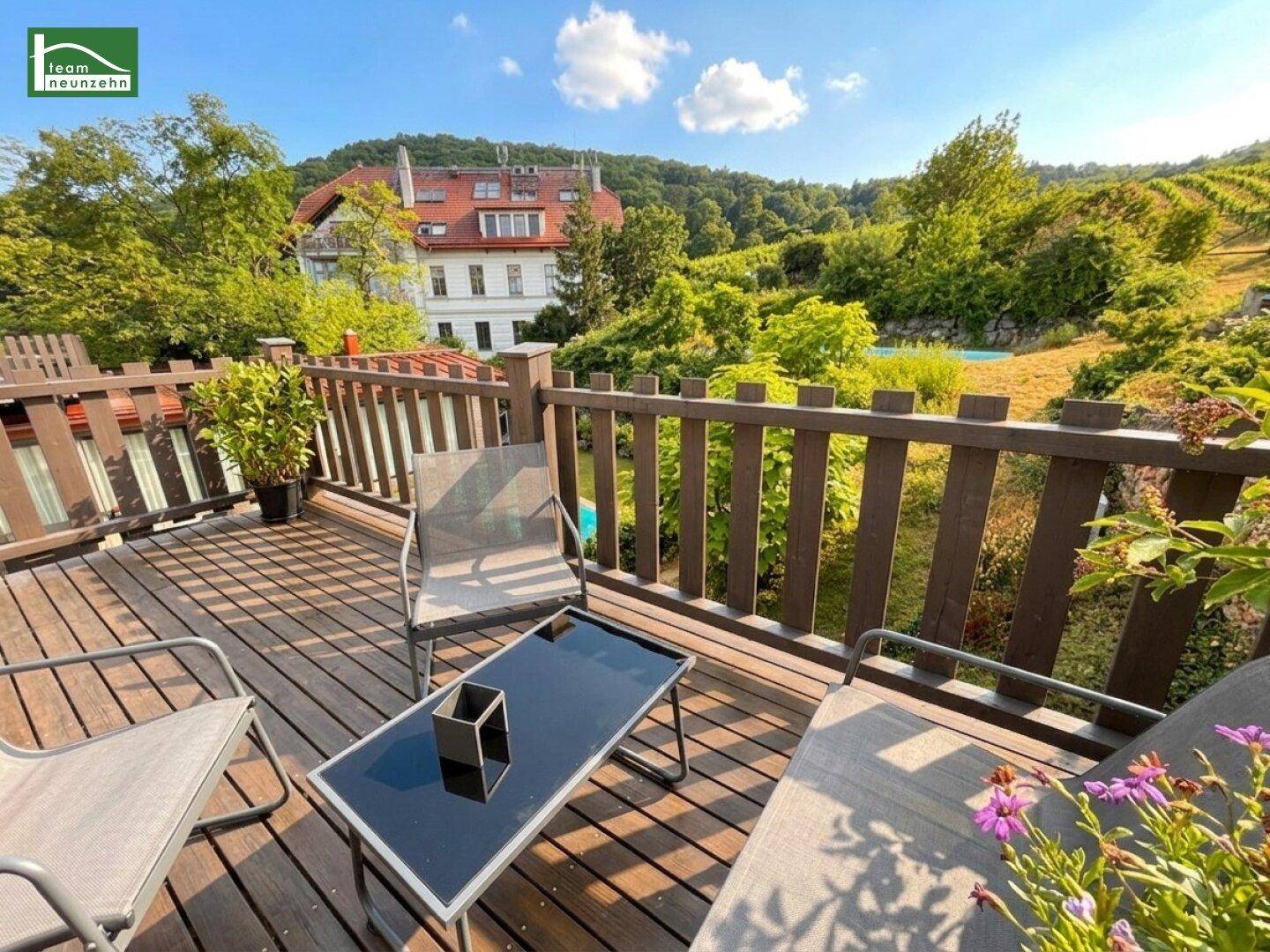 Sonniger Holzbalkon mit Gartenmöbeln und weitem Blick über die Landschaft und Weinberge.