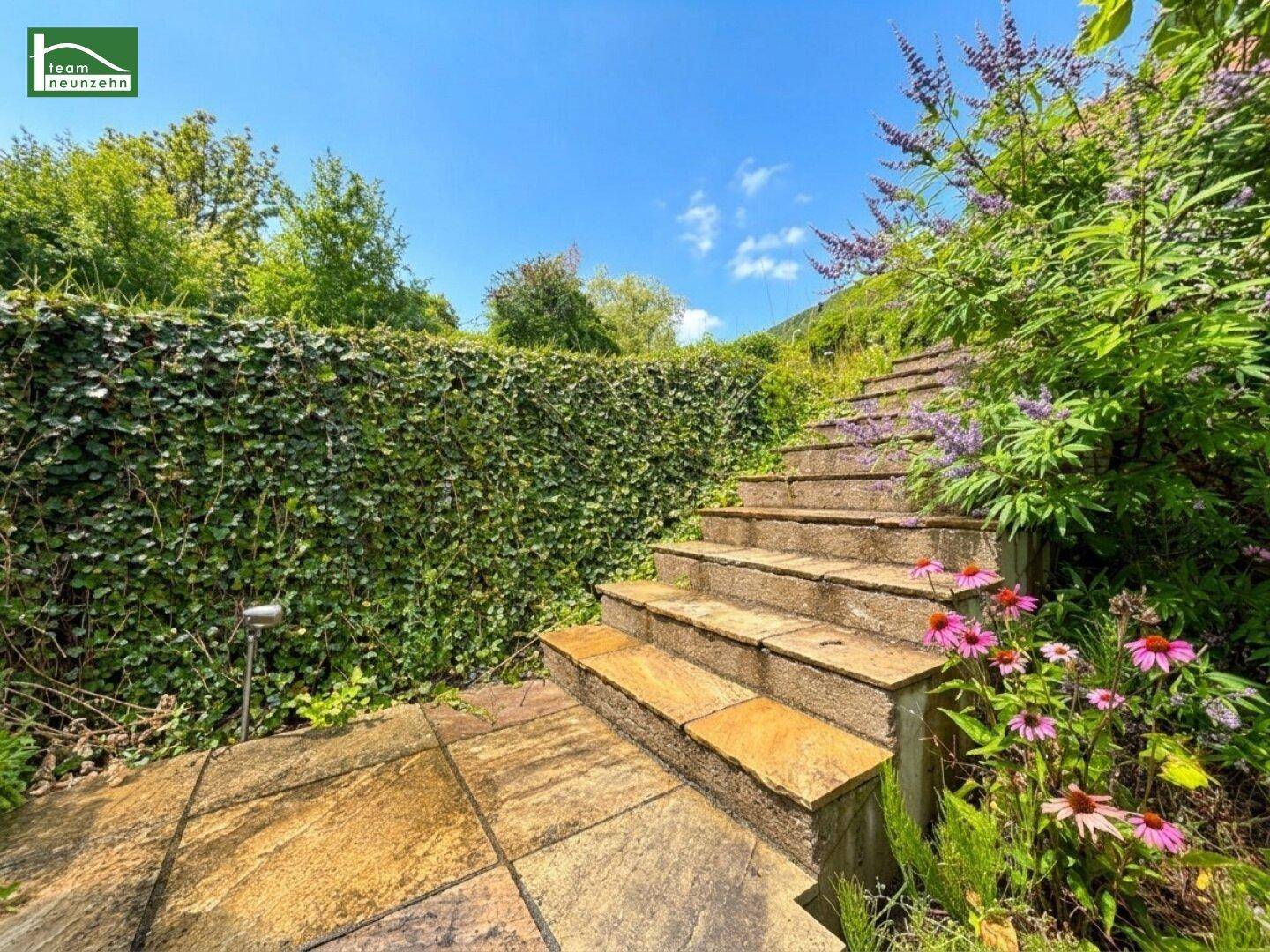 Steintreppe im Garten, umgeben von üppigem Grün und blühenden Pflanzen.