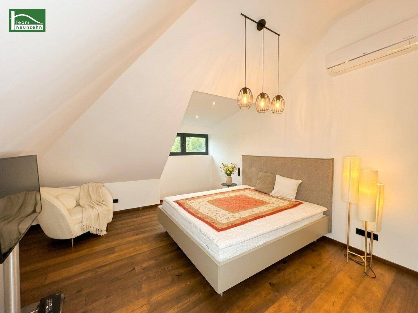 Helles Schlafzimmer mit Holzboden, Klimaanlage und schrägen Wänden unter dem Dach.