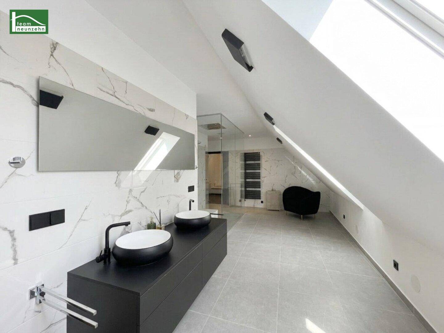Modernes Badezimmer mit Doppelwaschbecken, Marmorfliesen und Dachfenster unter einer Dachschräge.