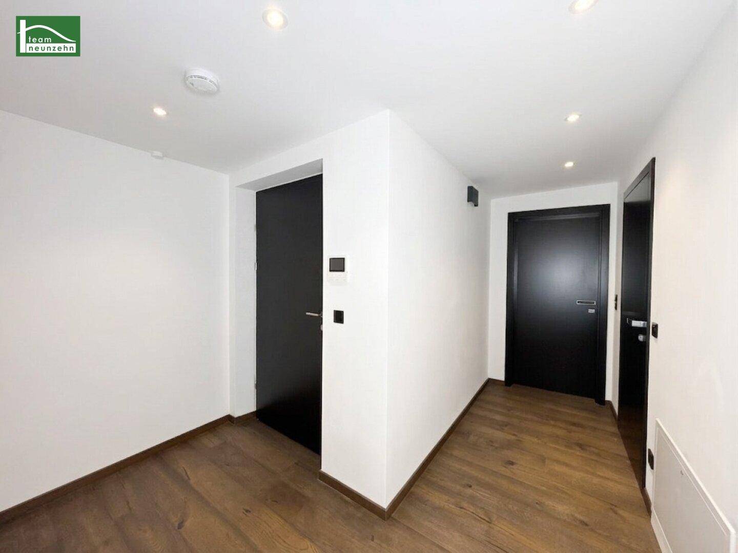 Heller Flur mit dunklen Türen und elegantem Holzboden.
