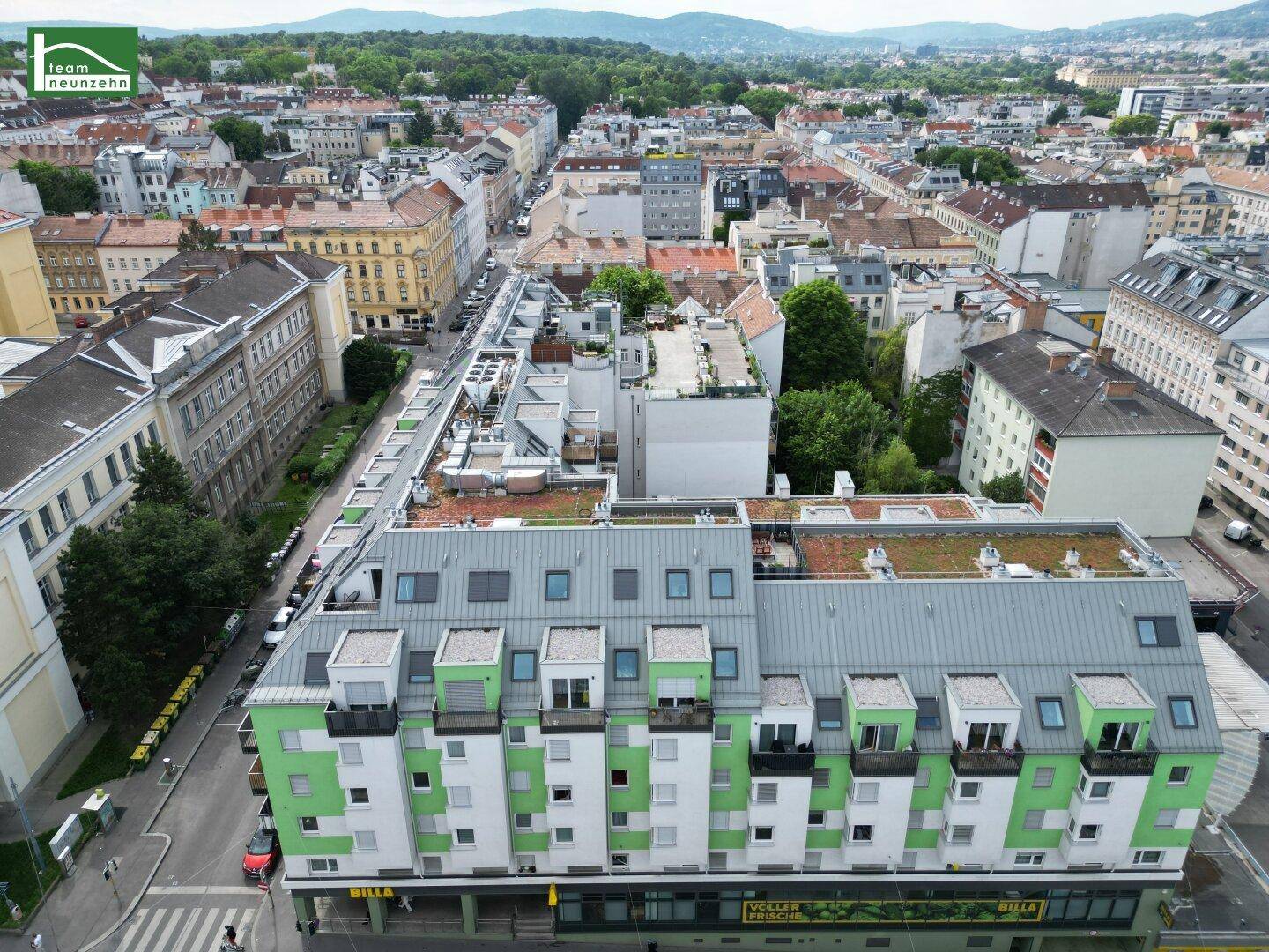 Luftaufnahme des Gebäudes mit seiner grün-weißen Fassade und der belebten Straße davor.