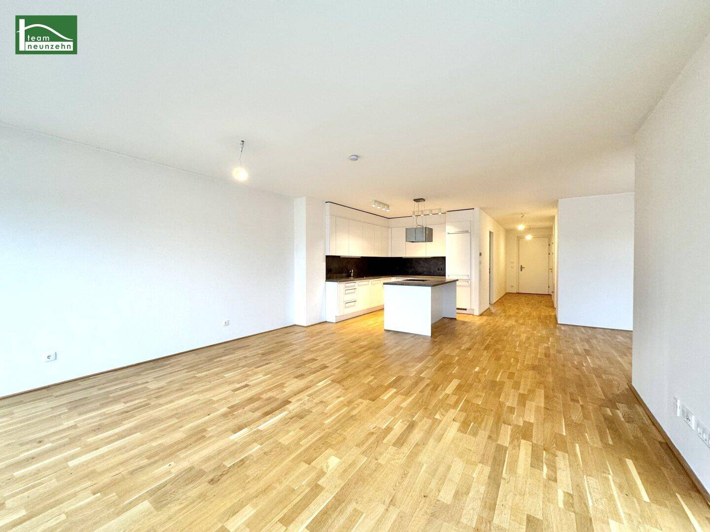 Offener Wohnbereich mit Holzboden und moderner Einbauküche im Hintergrund, ideal für geselliges Beisammensein.