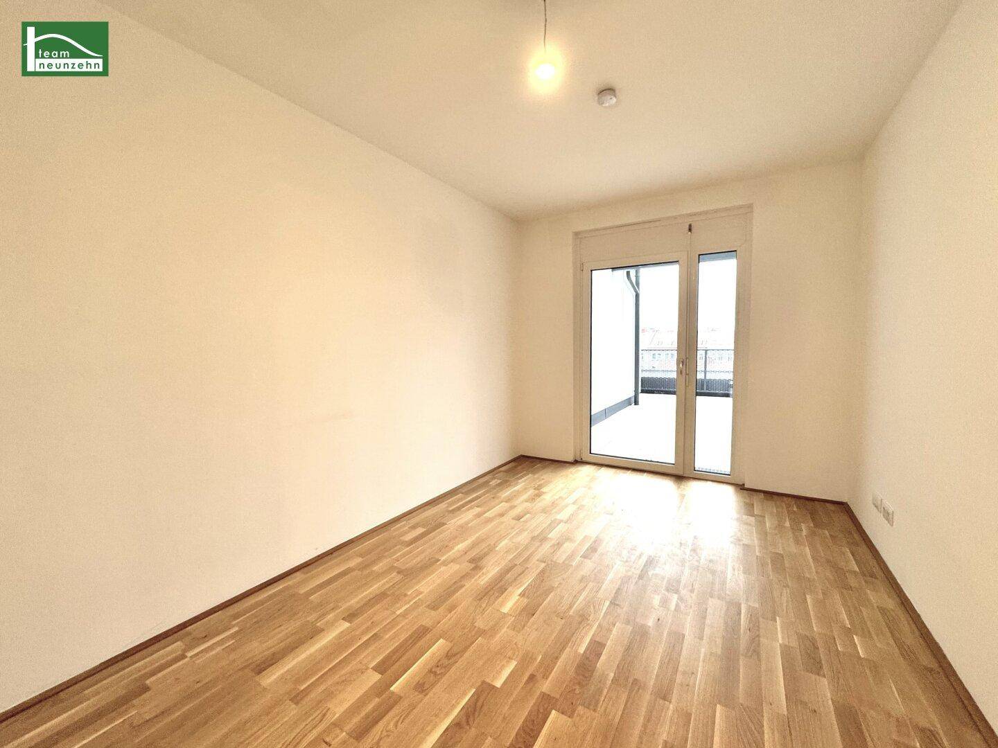 Leeres Zimmer mit Holzboden und Balkonzugang, das sich ideal als Schlaf- oder Arbeitszimmer eignet.
