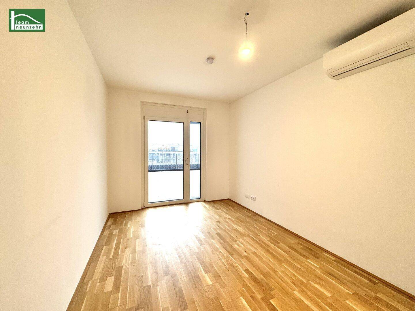 Helles Schlafzimmer mit Parkettboden, Zugang zum Balkon und installierter Klimaanlage.