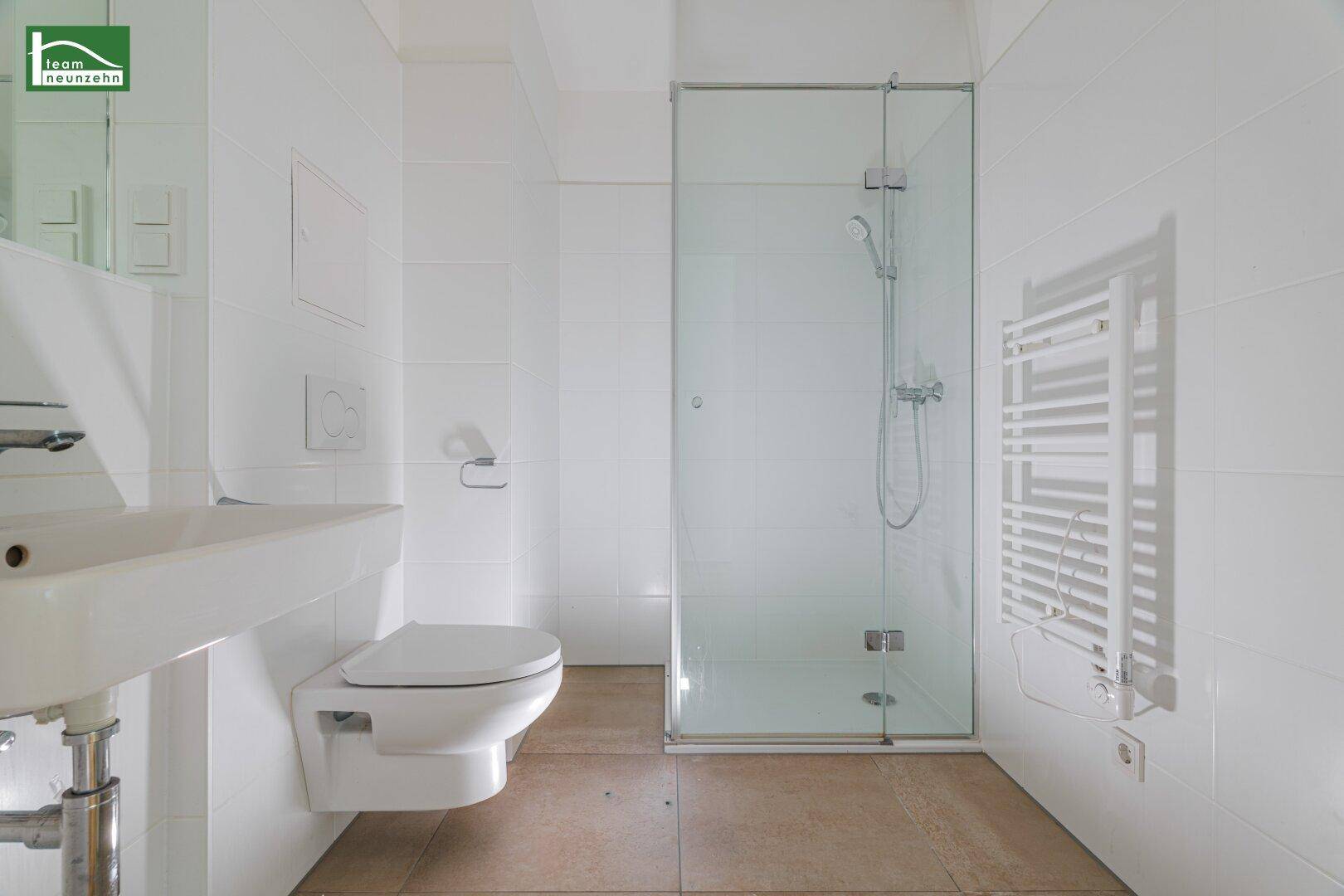 Modernes Badezimmer mit weißen Fliesen, Duschkabine, wandhängendem WC und Handtuchheizkörper.