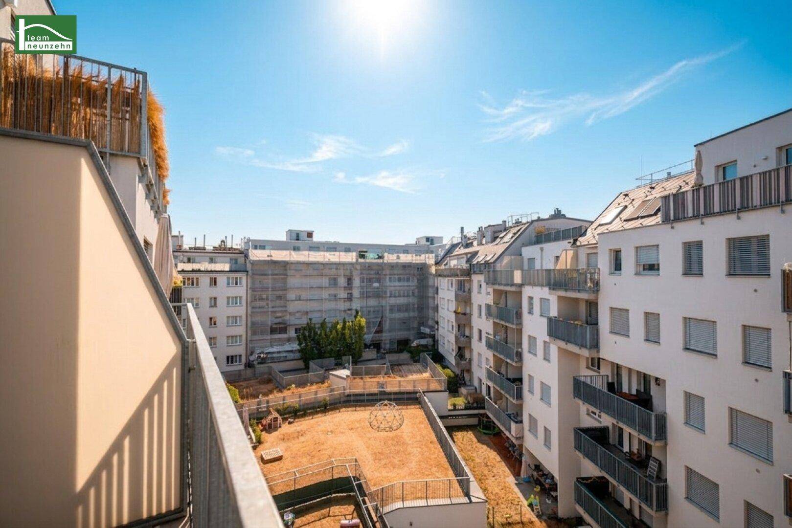 Weitblick vom Balkon auf die umliegenden Gebäude und einen Innenhofbereich unter blauem Himmel.