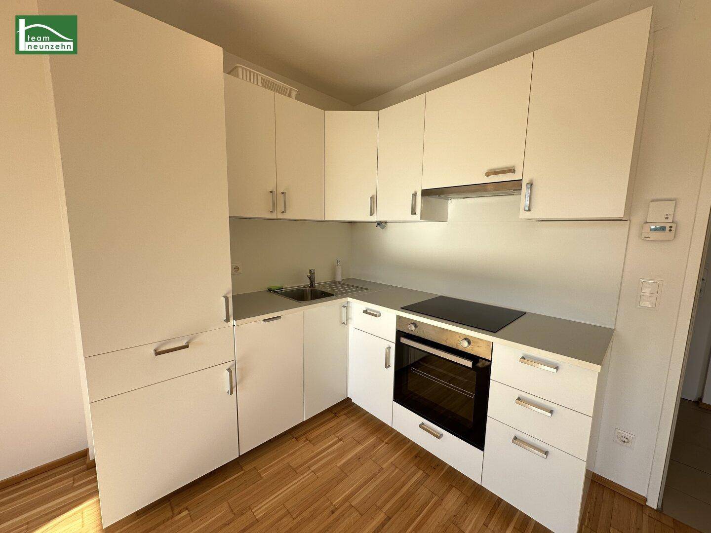 Moderne Küchenzeile mit weißen Schränken, integriertem Backofen und Induktionskochfeld, in gutem Zustand.