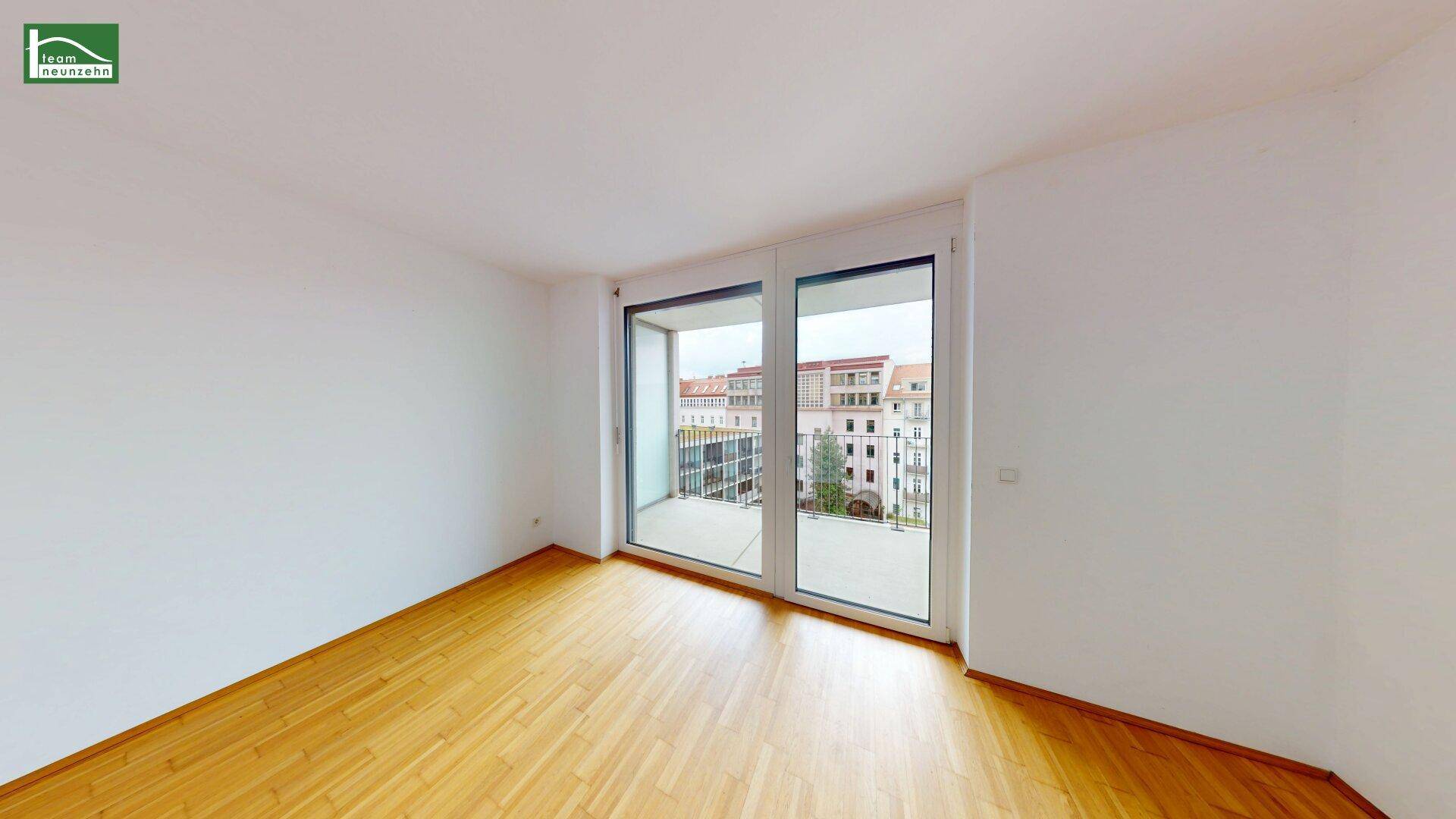 Helles Schlafzimmer mit Parkettboden und großem Fenster, das Zugang zu einem Balkon bietet.