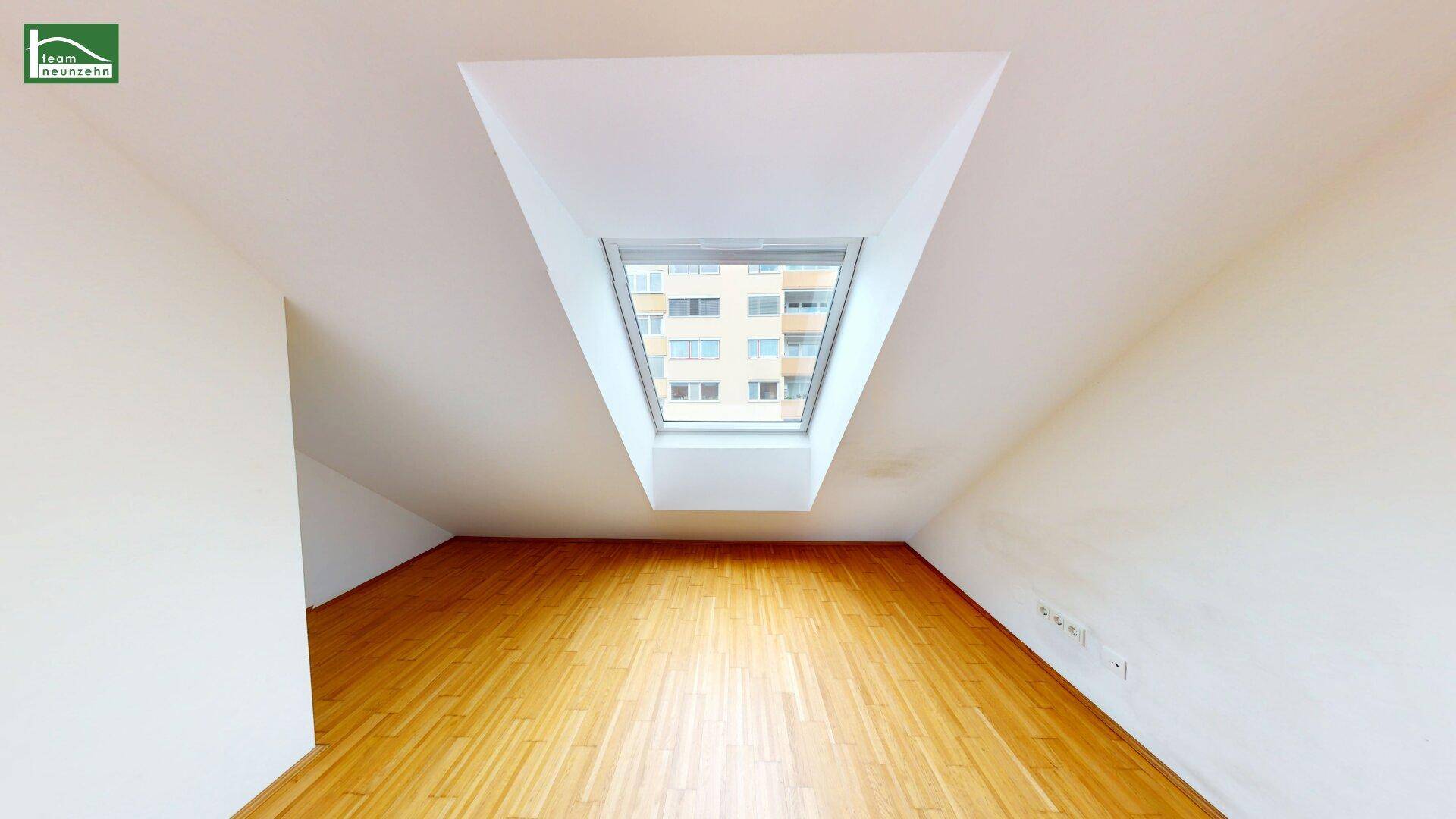 Leeres Schlafzimmer im Dachgeschoss mit schrägen Wänden und großem Dachfenster für viel Licht.