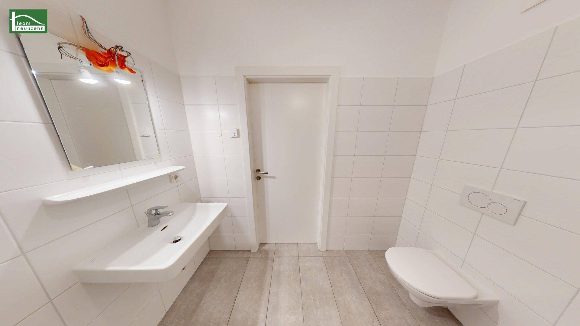 Helles Badezimmer mit Waschbecken, Spiegel und Toilette, ausgestattet mit weißen Fliesen.