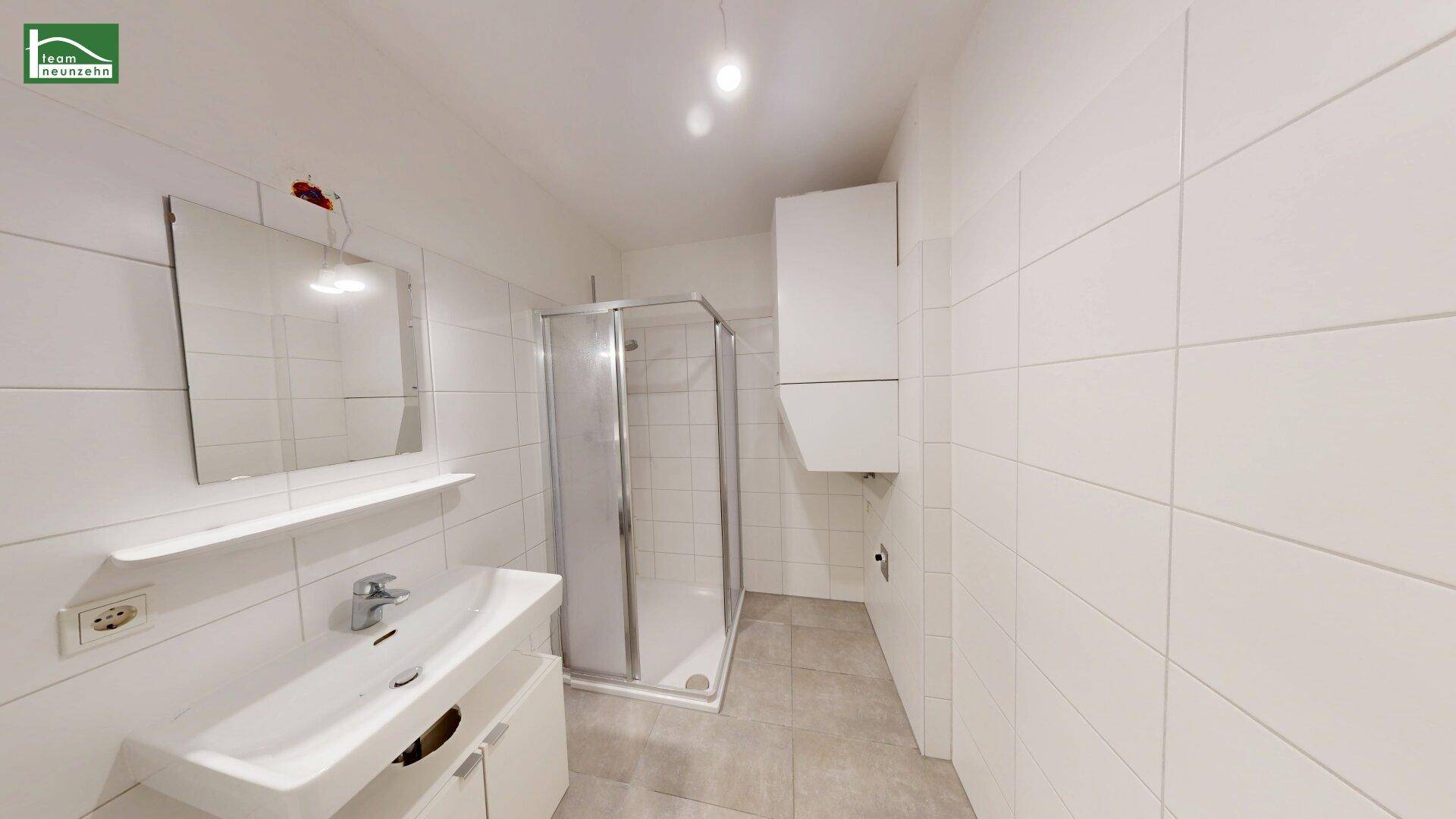 Modernes Badezimmer mit weißen Fliesen, Duschkabine und Waschbecken mit Unterschrank.