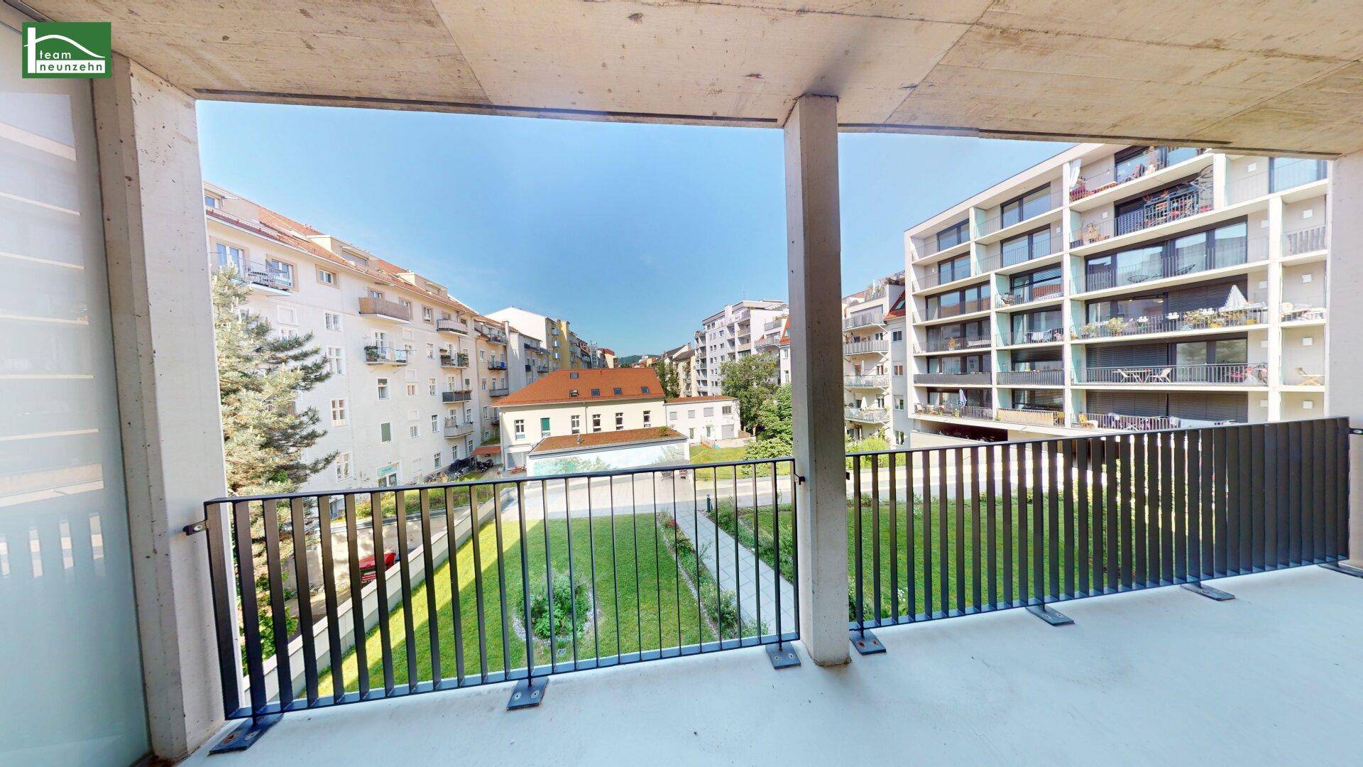 Breiter Balkon mit Blick auf einen begrünten Innenhof und die umliegende Stadtbebauung.