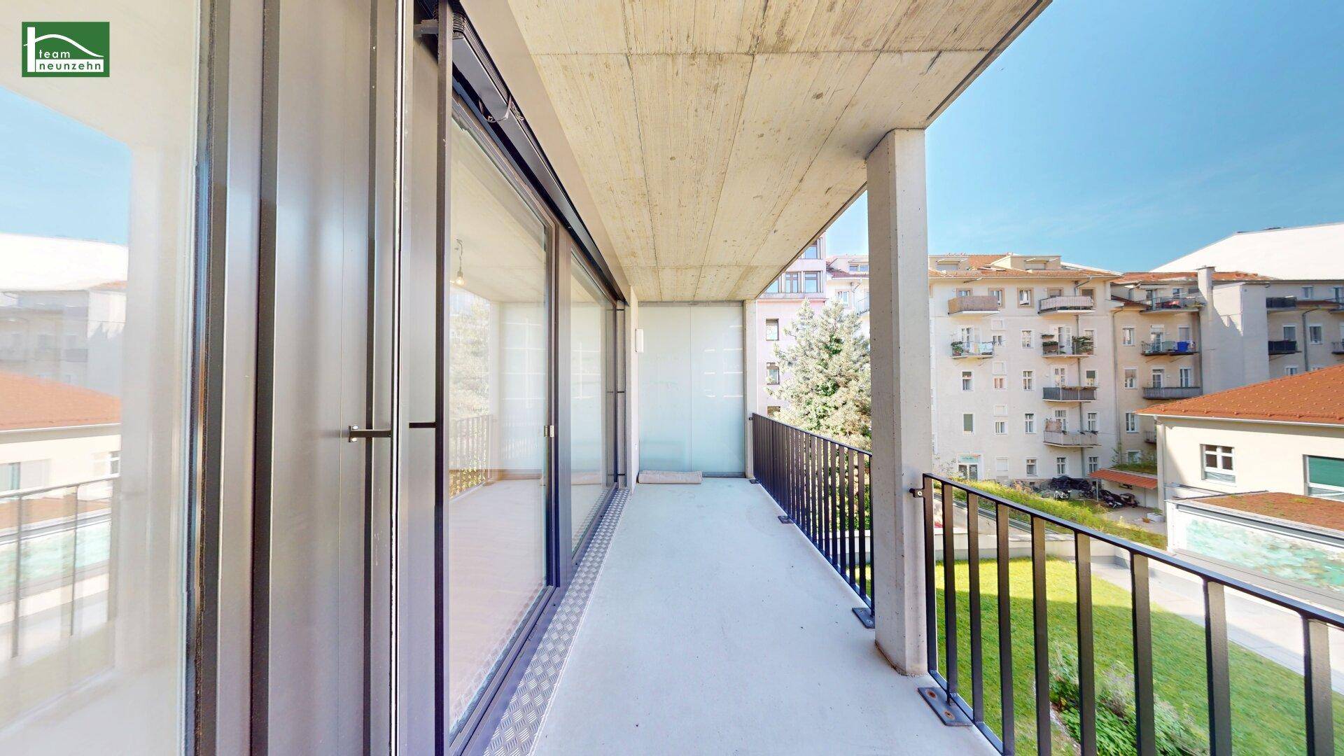 Geräumiger Balkon mit Betonboden und Metallgeländer, bietet einen Blick auf die umliegenden Gebäude.