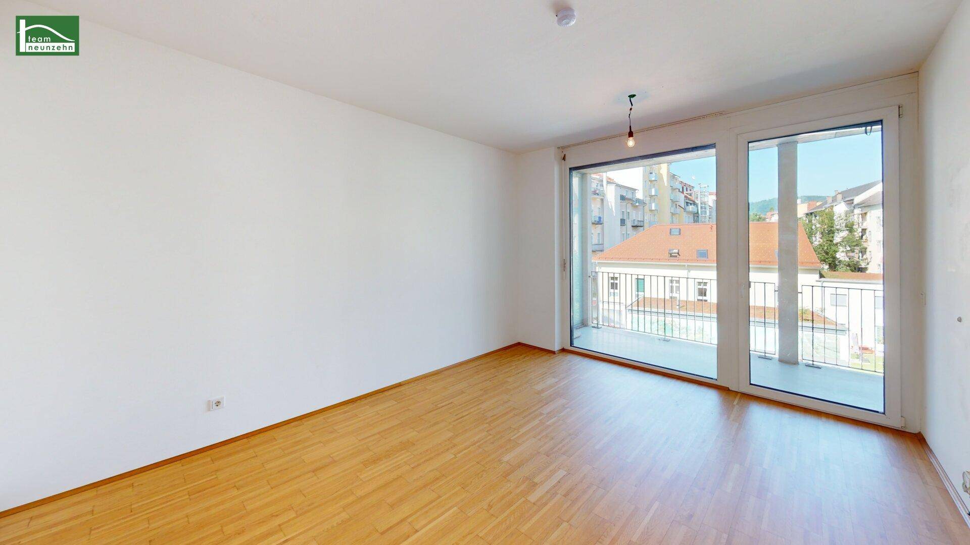 Geräumiges, unmöbliertes Zimmer mit Holzboden und großen Fenstern, die viel Tageslicht hereinlassen.