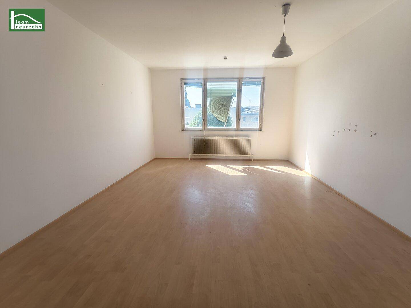 Sonniges Zimmer mit Laminatboden und Heizkörper unter dem Fenster.