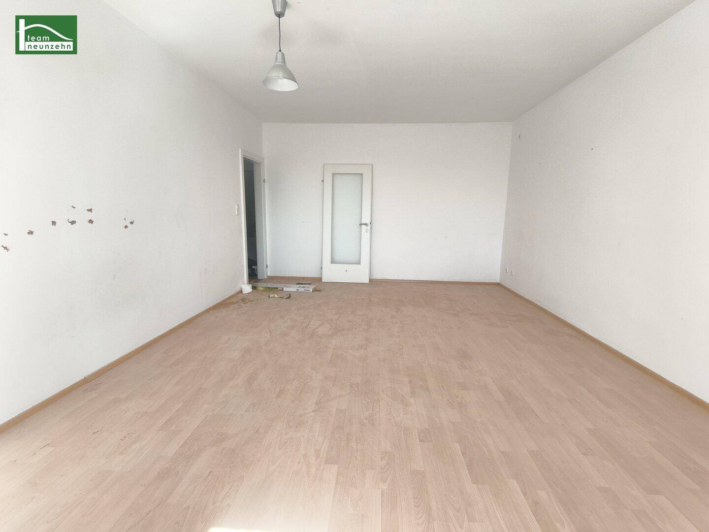 Helles Zimmer mit Laminatboden und einer Tür mit Glaseinsatz.