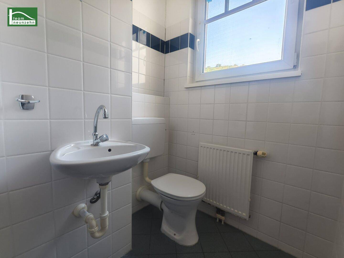 Badezimmer mit WC, Waschbecken und Fenster, gefliest in Weiß mit blauen Akzenten.