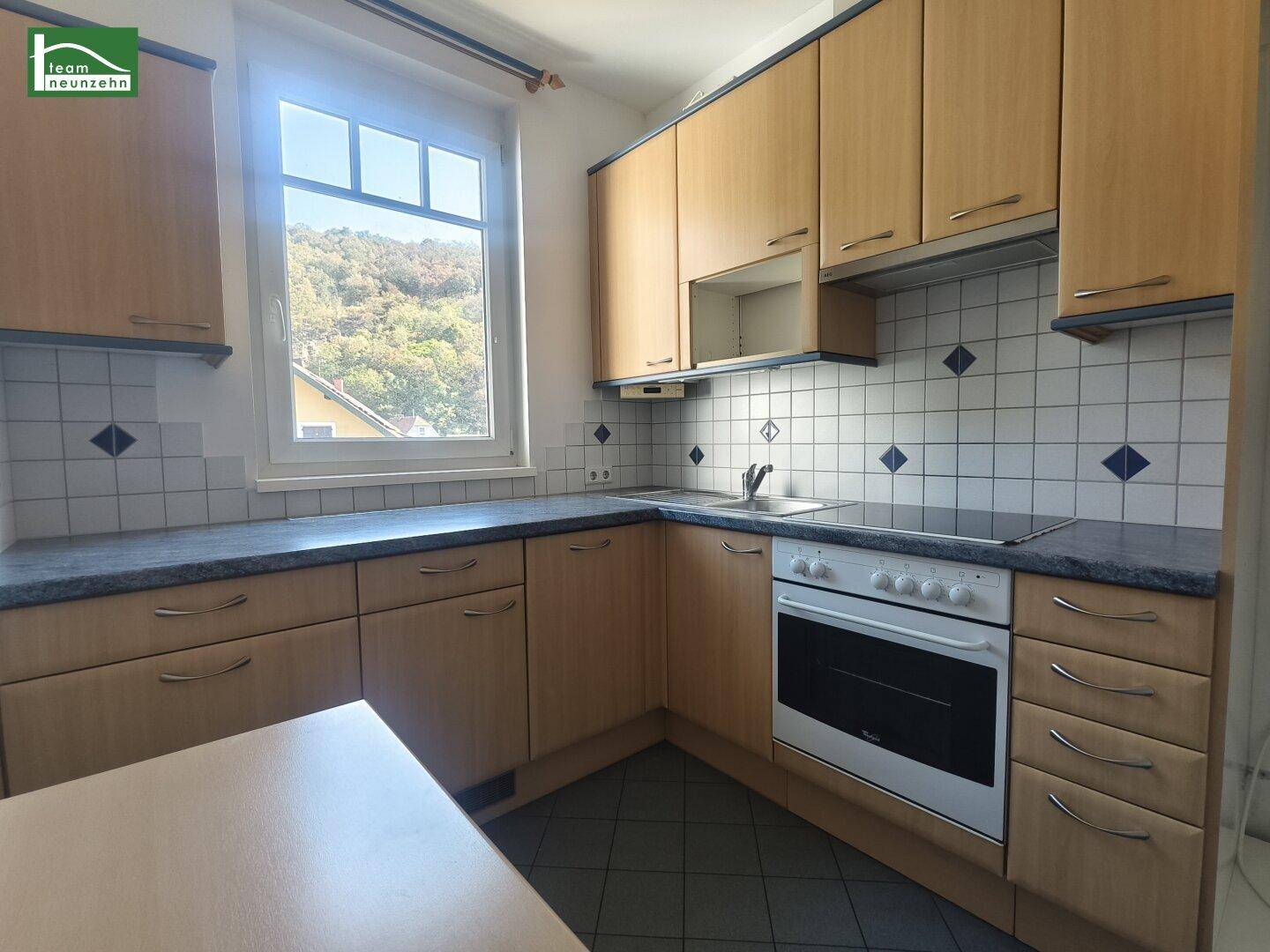 Funktionale Küche mit Holzschränken, Fliesenrückwand und Blick ins Grüne vom Fenster aus.