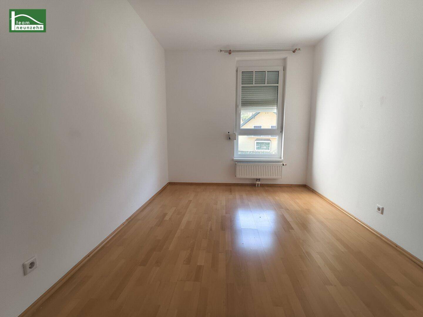 Helles Zimmer mit Parkettboden und Fenster, das eine angenehme Wohnatmosphäre schafft.