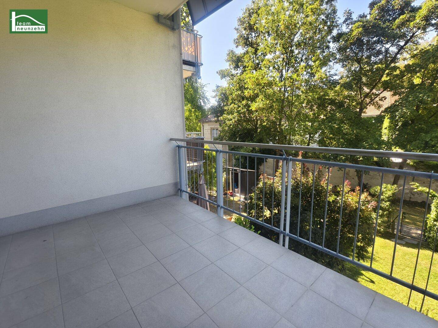 Geräumiger Balkon mit Fliesen und Blick auf den Gartenbereich mit Bäumen und Rasen.