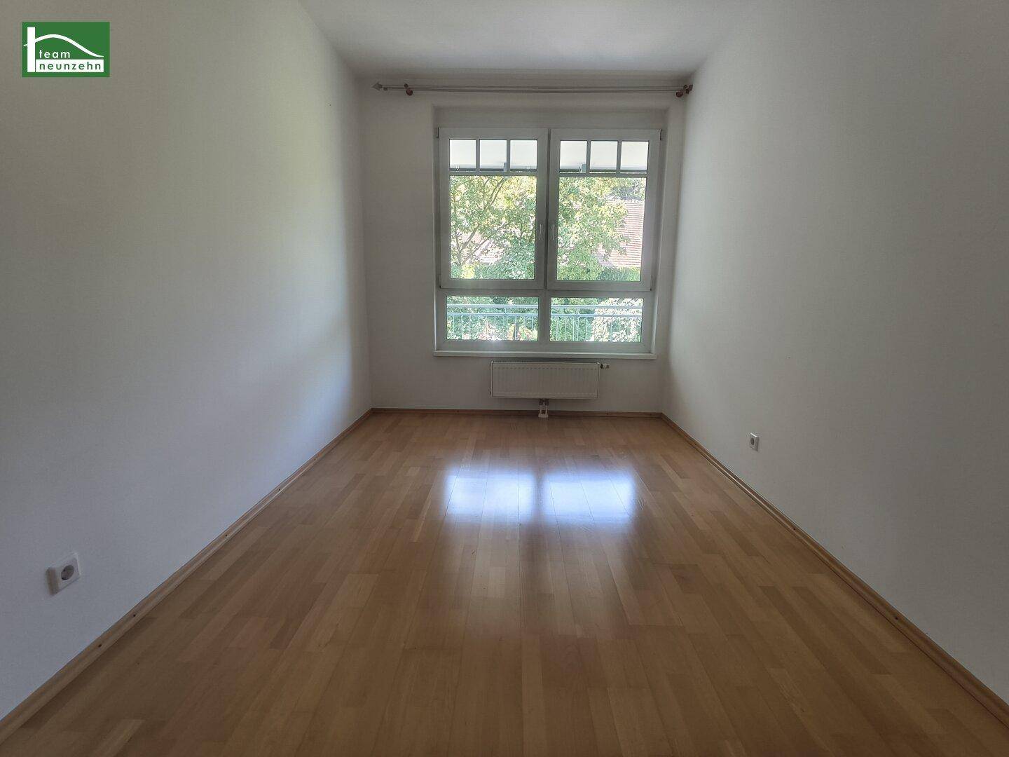 Helles Zimmer mit Parkettboden und Fenster, das viel Tageslicht hereinlässt.